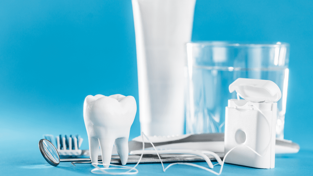 The image shows various dental care items against a blue background, including a model of a tooth, dental floss, a toothbrush, a dental mirror, and a glass of water. These items are commonly used for oral hygiene and dental check-ups.